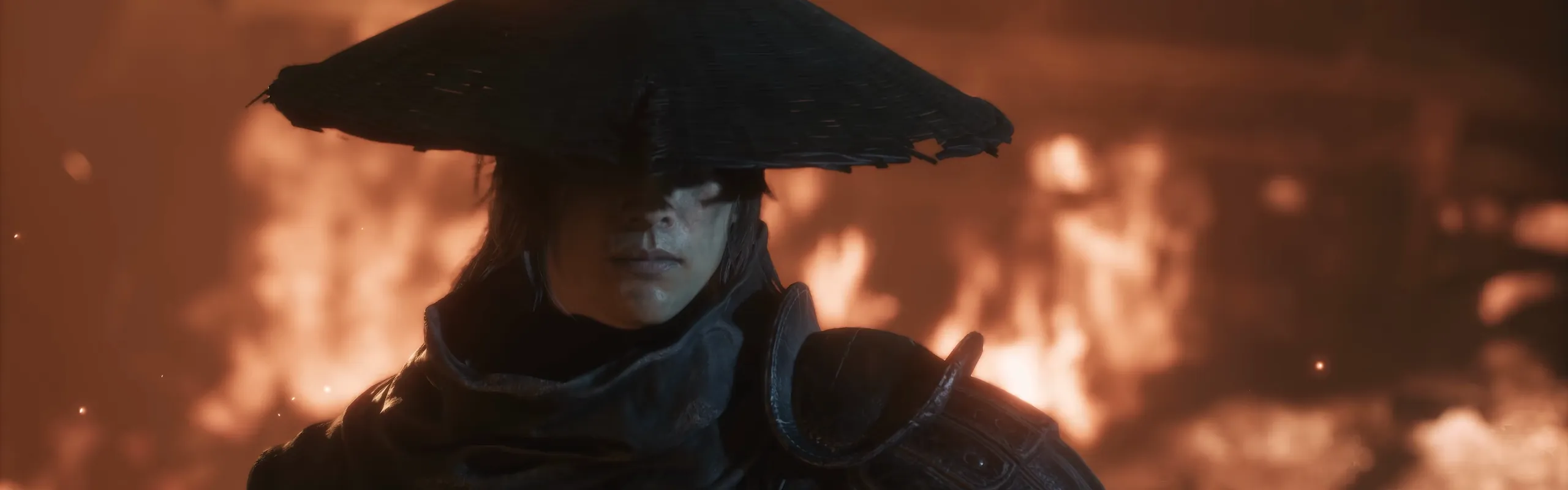 A man in a wide straw hat and dark armour stands before a wall of flames.