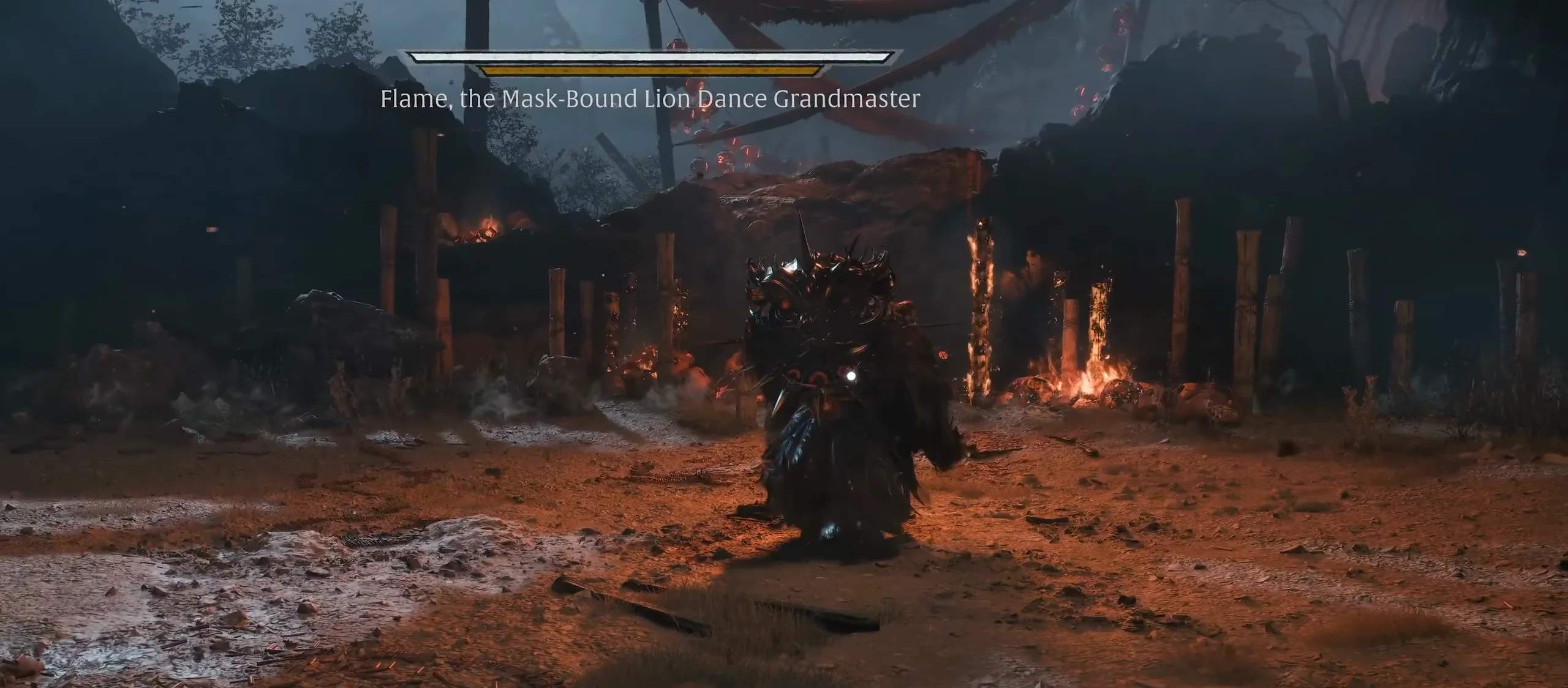 A huge figure in a spiked lion-head mask stands in a yard of red earth before burning wooden posts, under a name plate.